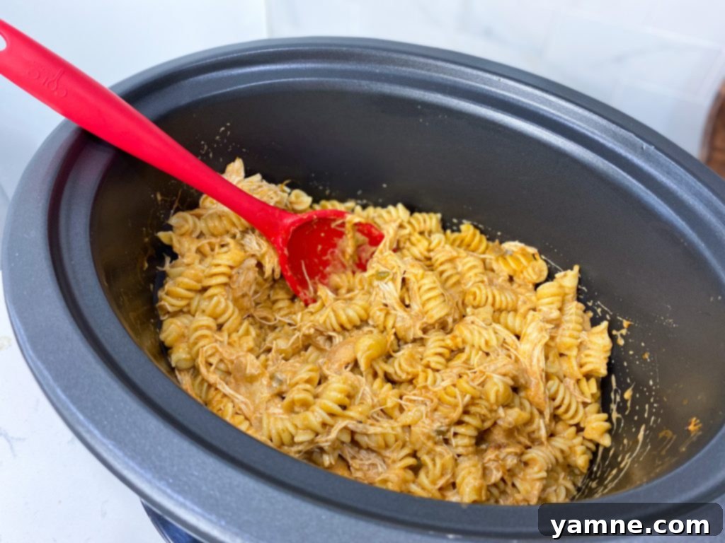 Cheesy Crockpot Enchilada Pasta 4 Serving of slow cooker chicken enchilada pasta in a bowl, topped with shredded cheese and a dollop of sour cream.