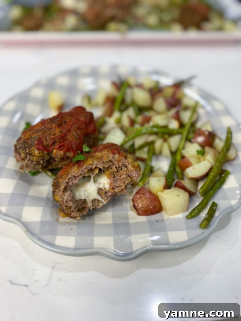 One-Pan Cheesy Stuffed Meatloaf and Roasted Veggies 4 A close-up of a perfectly cooked mozzarella stuffed meatloaf, with melted cheese peeking out, served on a plate.