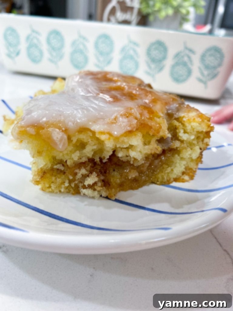 A delicious slice of Honey Bun Cake with a cinnamon swirl and vanilla glaze.