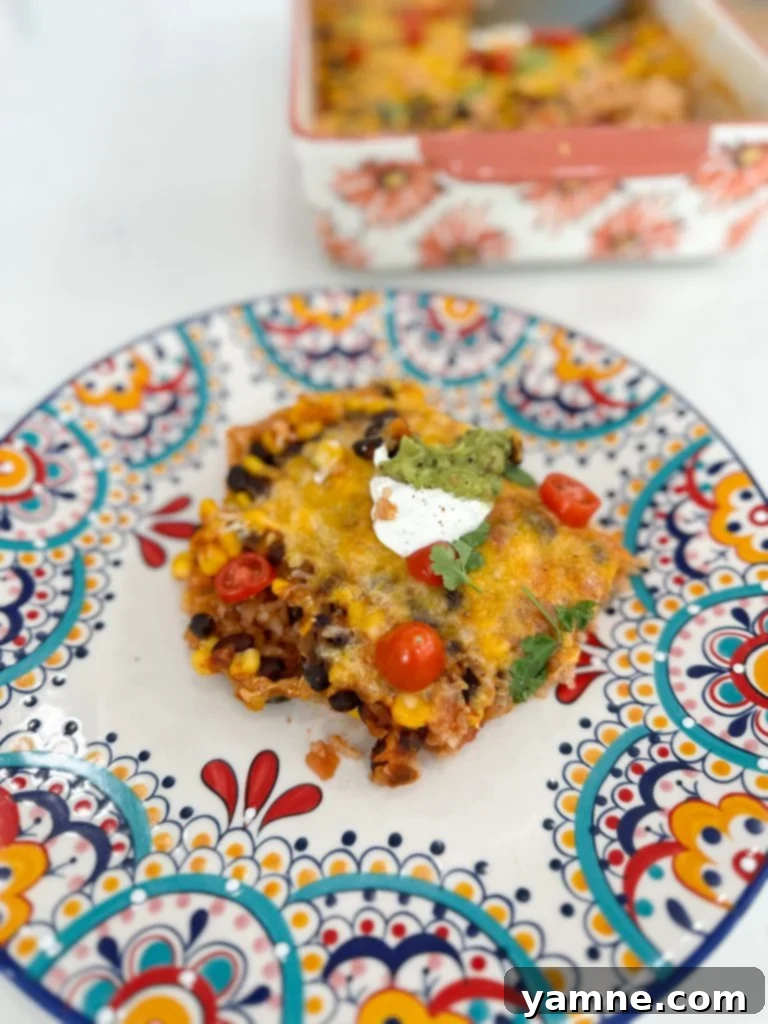Fiesta Veggie Casserole 4 A serving of the Vegetarian Mexican Casserole on a plate, topped with fresh avocado slices and a dollop of sour cream, with the rest of the casserole in the background.