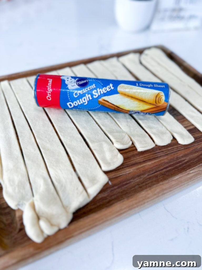 Unrolled crescent dough sheet and cut into strips on a cutting board.