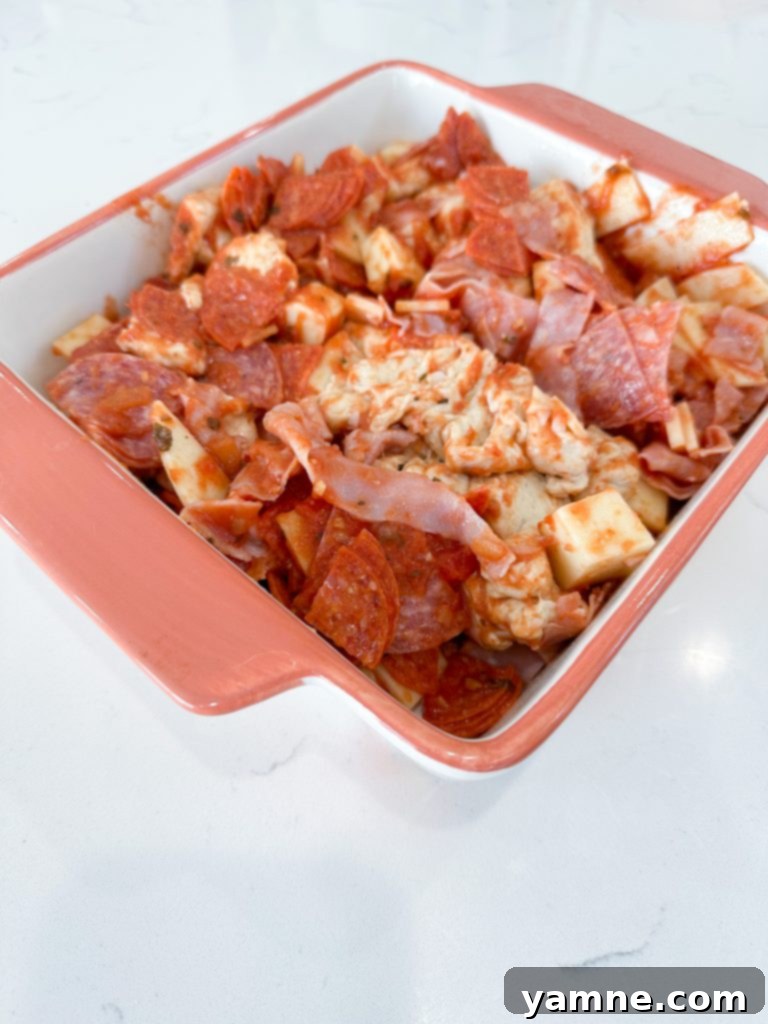 Mixing bowl with casserole ingredients - biscuits, meats, cheese, and marinara sauce combined.