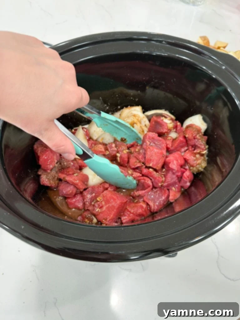 Steak and seasonings being mixed in a slow cooker.
