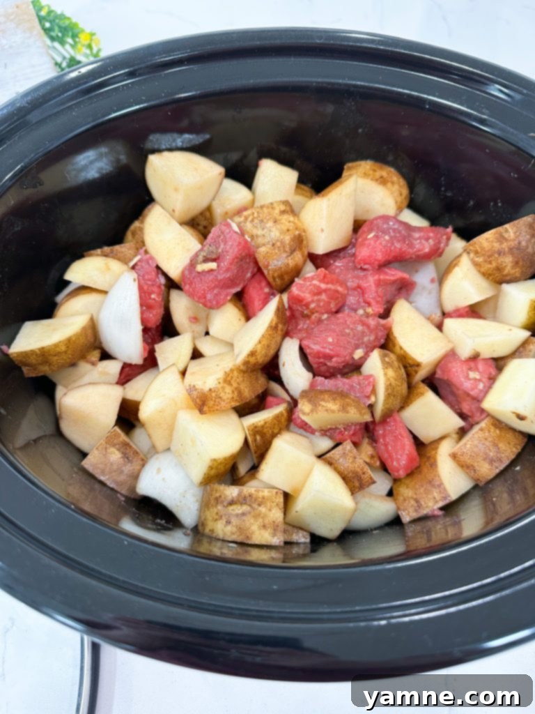 Potatoes added to the slow cooker with beef and seasonings.