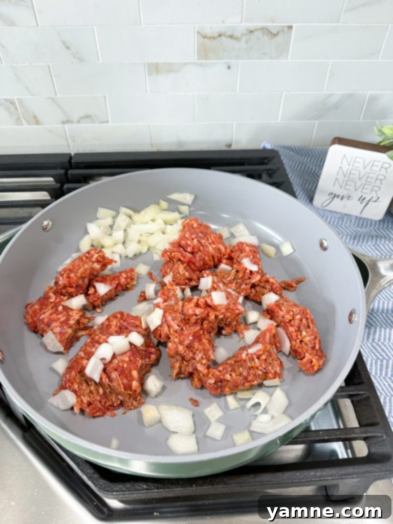 Effortless Slow Cooker Sausage Tortellini Lasagna 3 Italian sausage and diced yellow onion browning in a skillet, being broken up with a meat chopper.