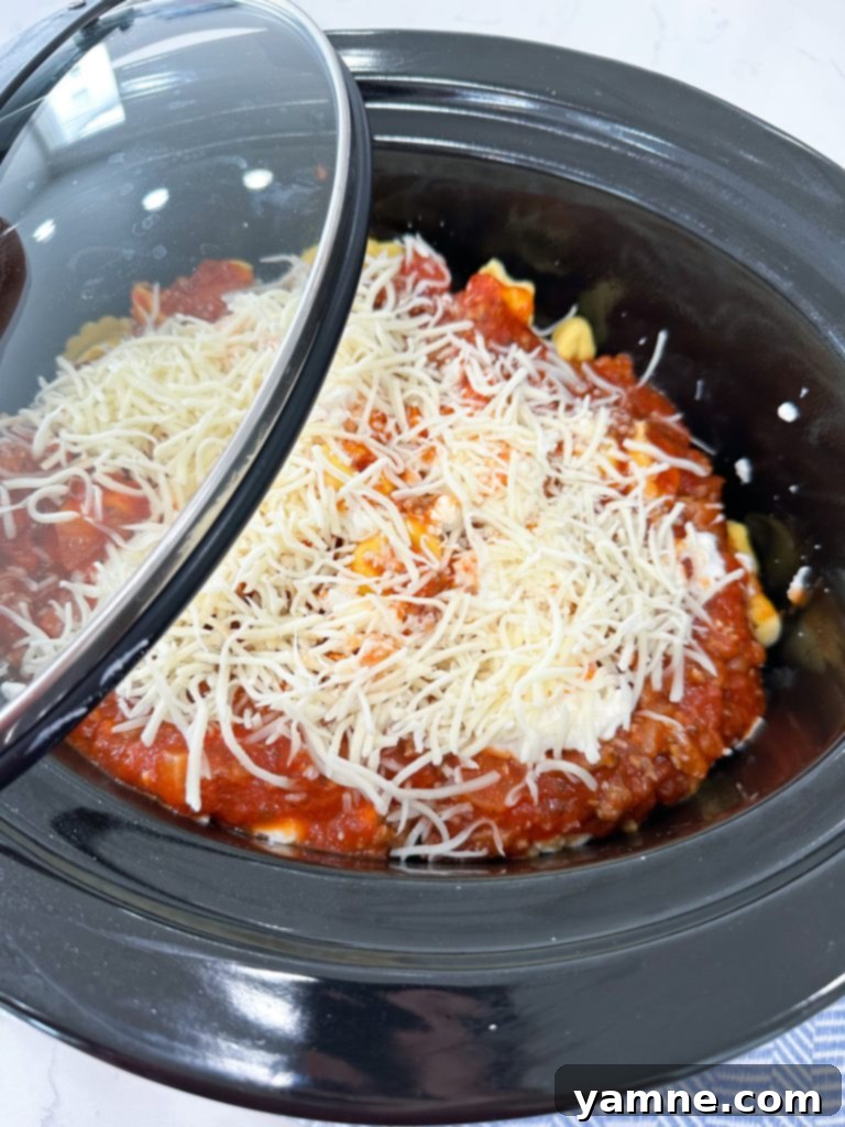 Effortless Slow Cooker Sausage Tortellini Lasagna 6 Layers of marinara sauce, cheese tortellini, and creamy cheese mixture visible in a slow cooker.