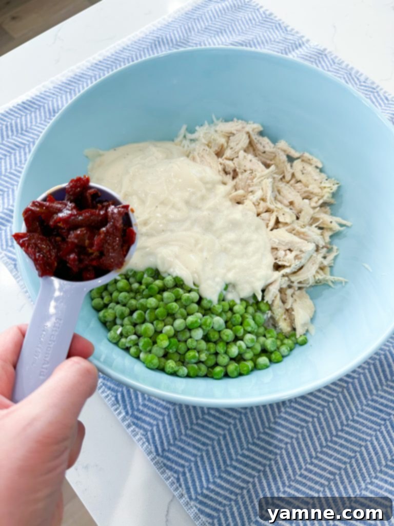Adding frozen peas and sun-dried tomatoes to the casserole ingredients.