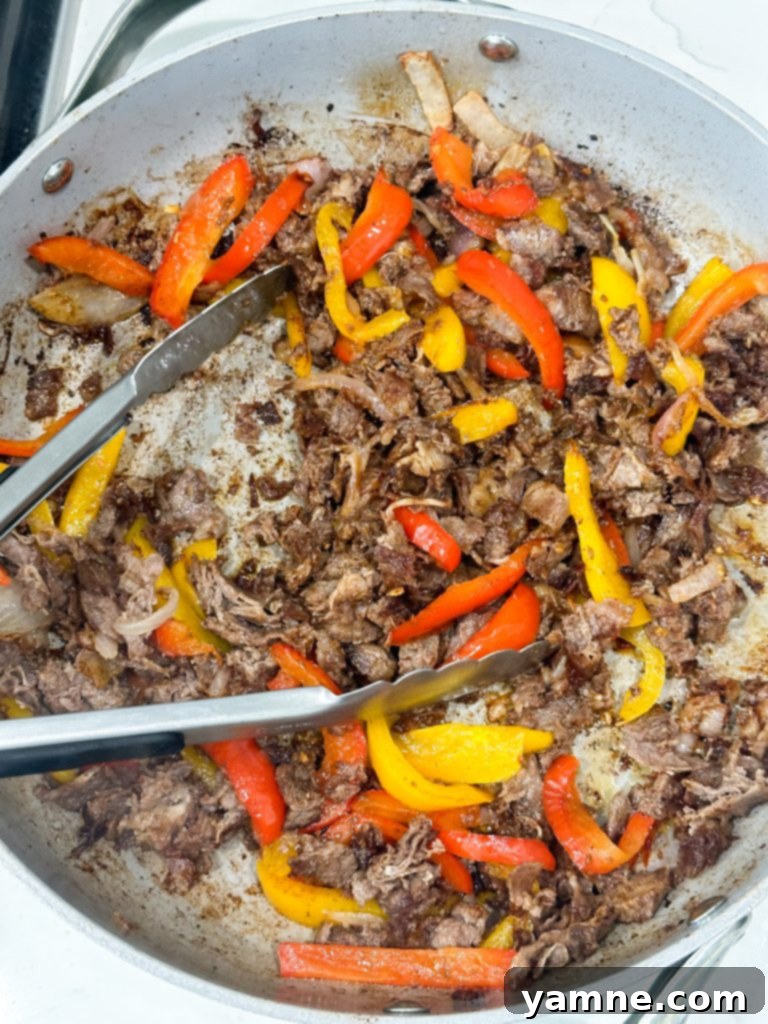 Sizzling steak and bell peppers cooking in a large skillet for the fajita quesadilla filling