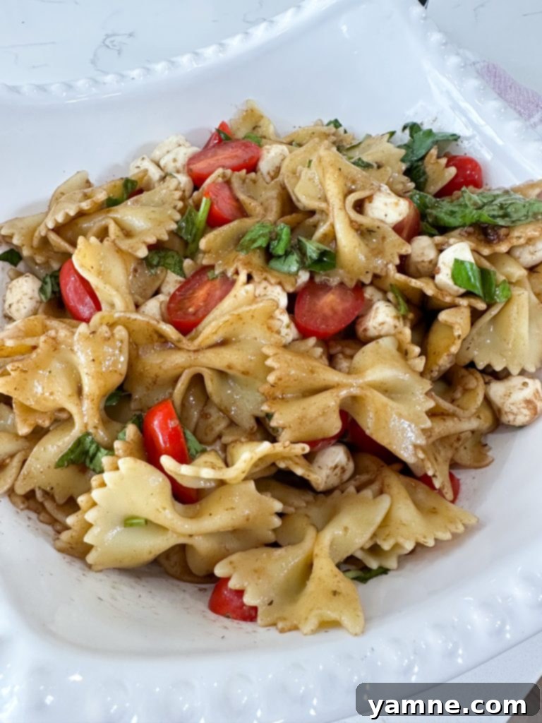 A beautifully arranged Caprese Pasta Salad with fresh basil, cherry tomatoes, and mozzarella pearls, drizzled with balsamic glaze.