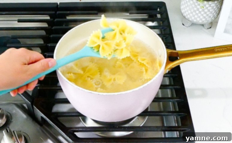 Pasta being rinsed under cold water in an over-the-sink strainer.