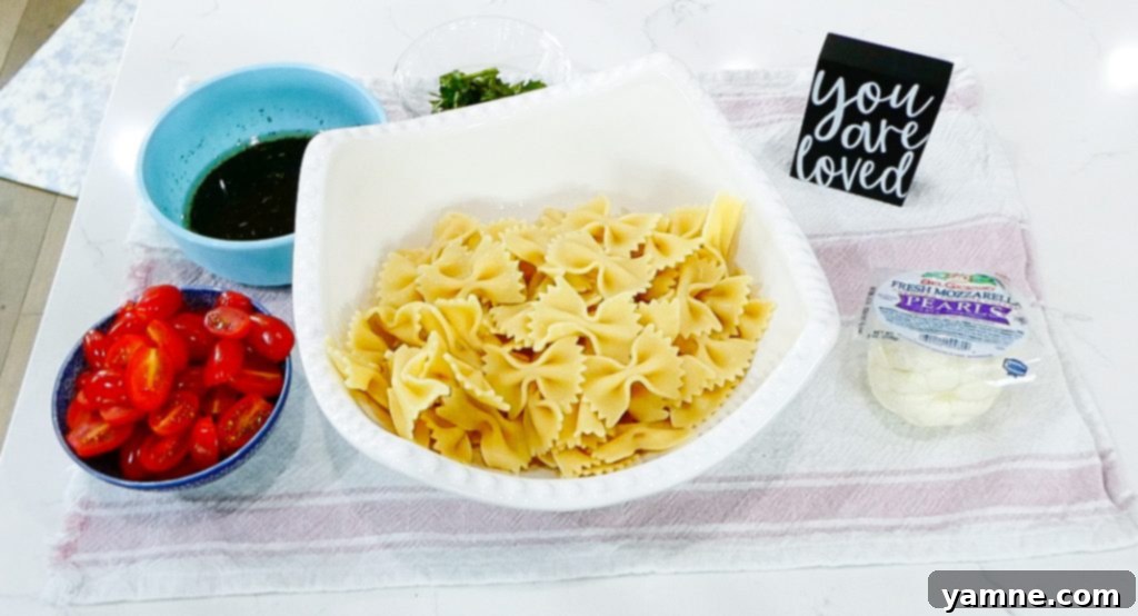 Cherry tomatoes, mozzarella pearls, and fresh basil added to the bowl with pasta.