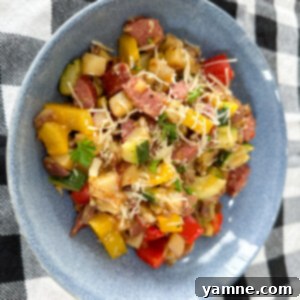 Roasted Sausage and Potatoes with Seasonal Vegetables 2 A vibrant one-pan dish of sliced kielbasa sausage, diced red potatoes, and colorful summer vegetables like zucchini and bell peppers, garnished with fresh herbs.