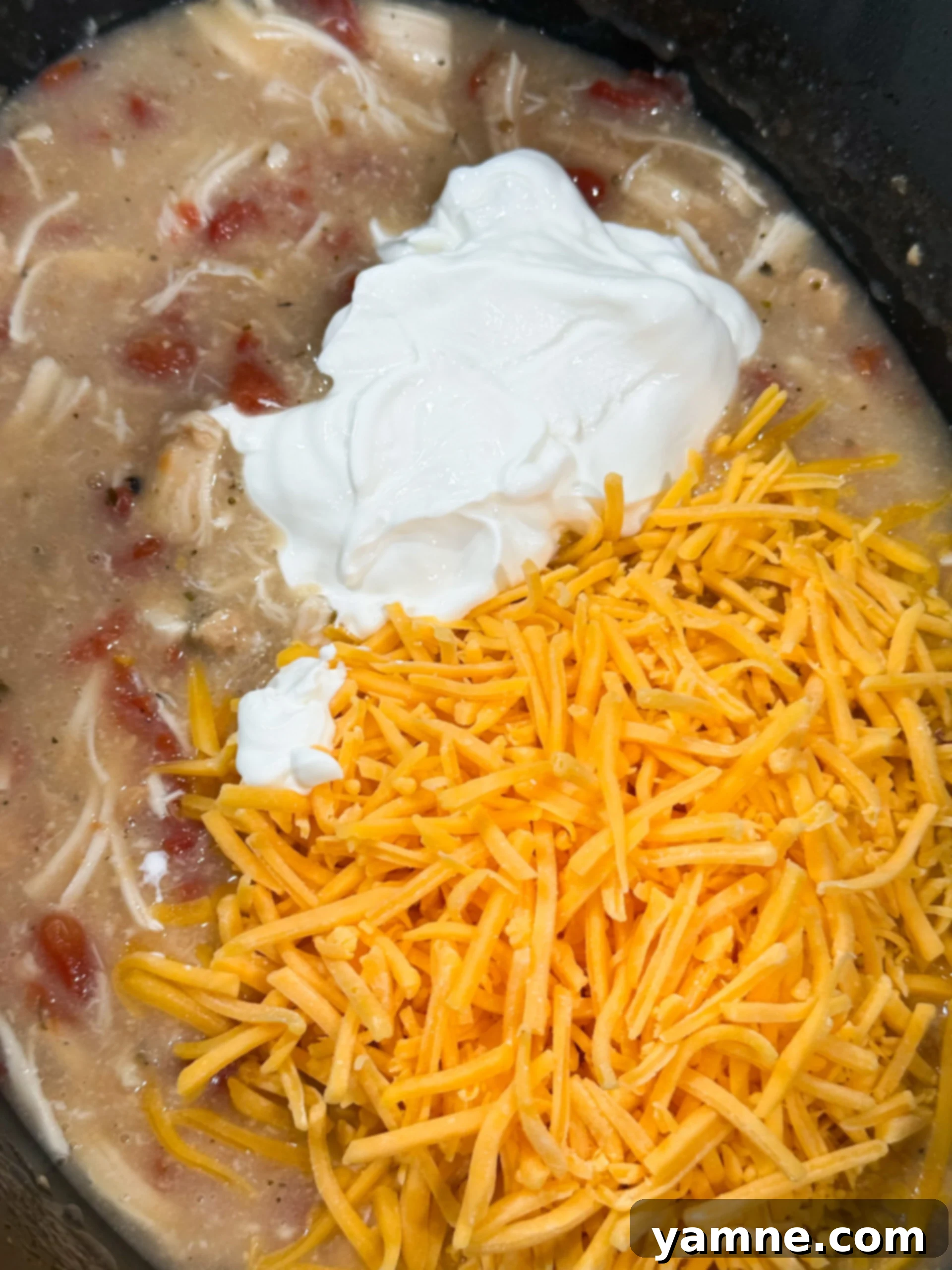 Easy Slow Cooker Creamy Rotel Chicken Pasta 8 Cheese and sour cream being added to slow cooker chicken mixture