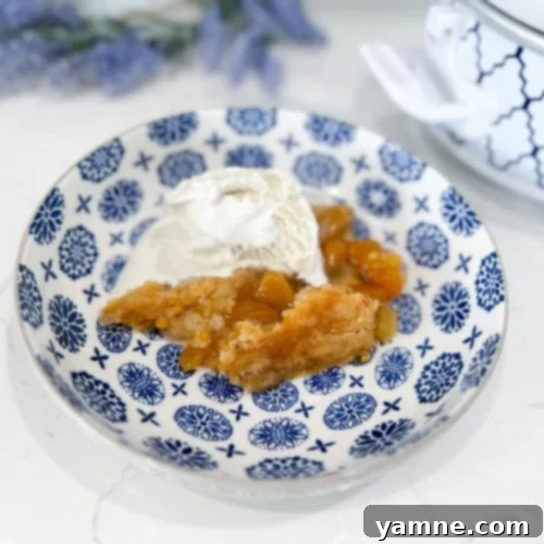 Slow cooker peach cobbler served warm with vanilla ice cream on top, showcasing its golden-brown topping and juicy peach filling.