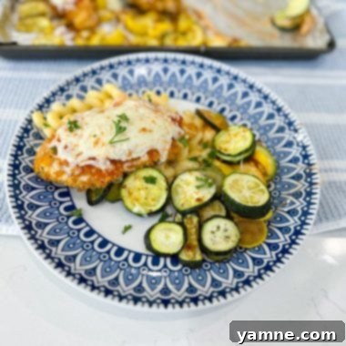 Crispy breaded chicken breasts topped with marinara and melted mozzarella cheese, served with roasted zucchini and yellow squash on a single sheet pan, ready to eat.