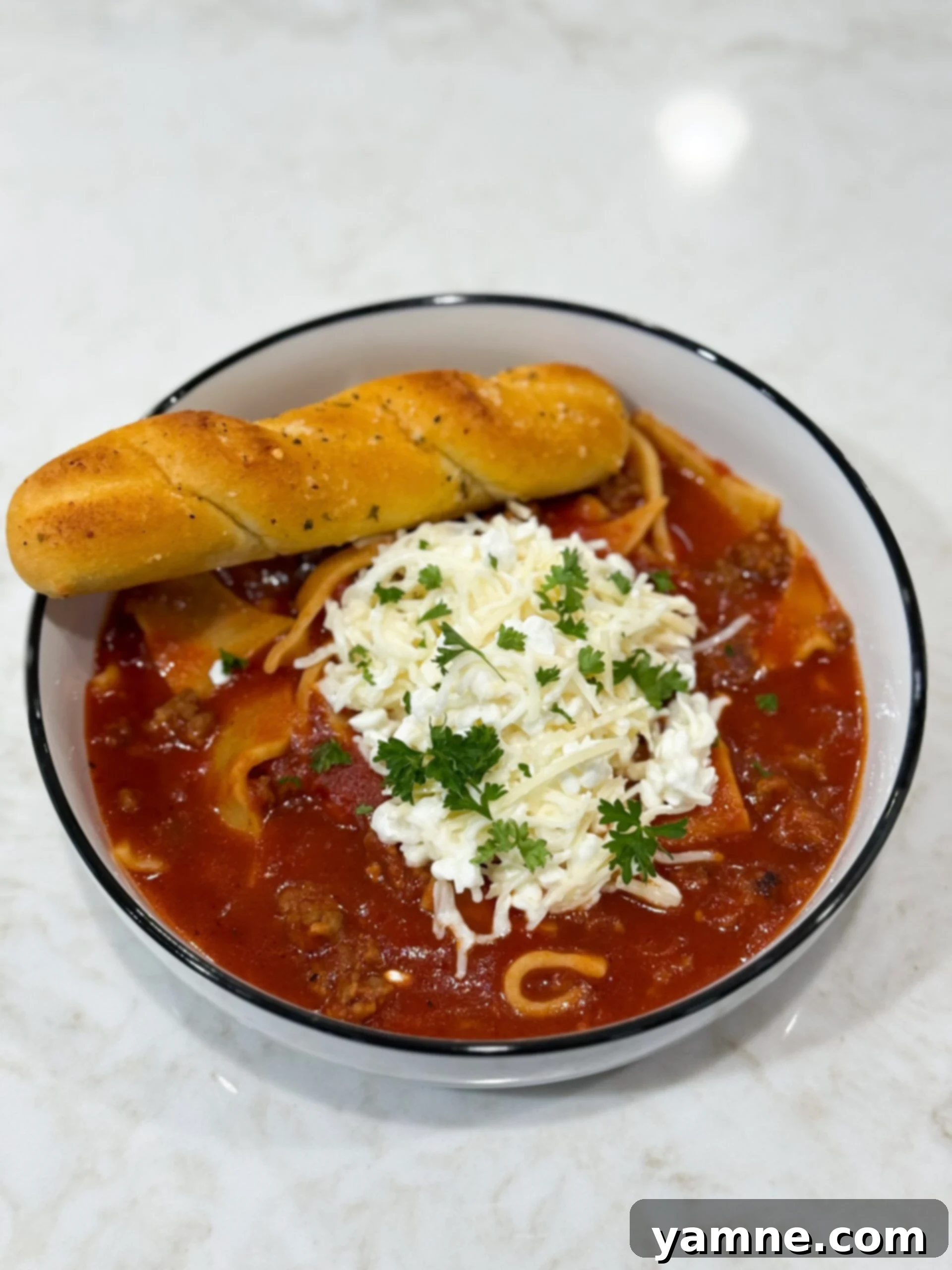 Slow cooker lasagna soup in bowl with with breadsticks and cheese.