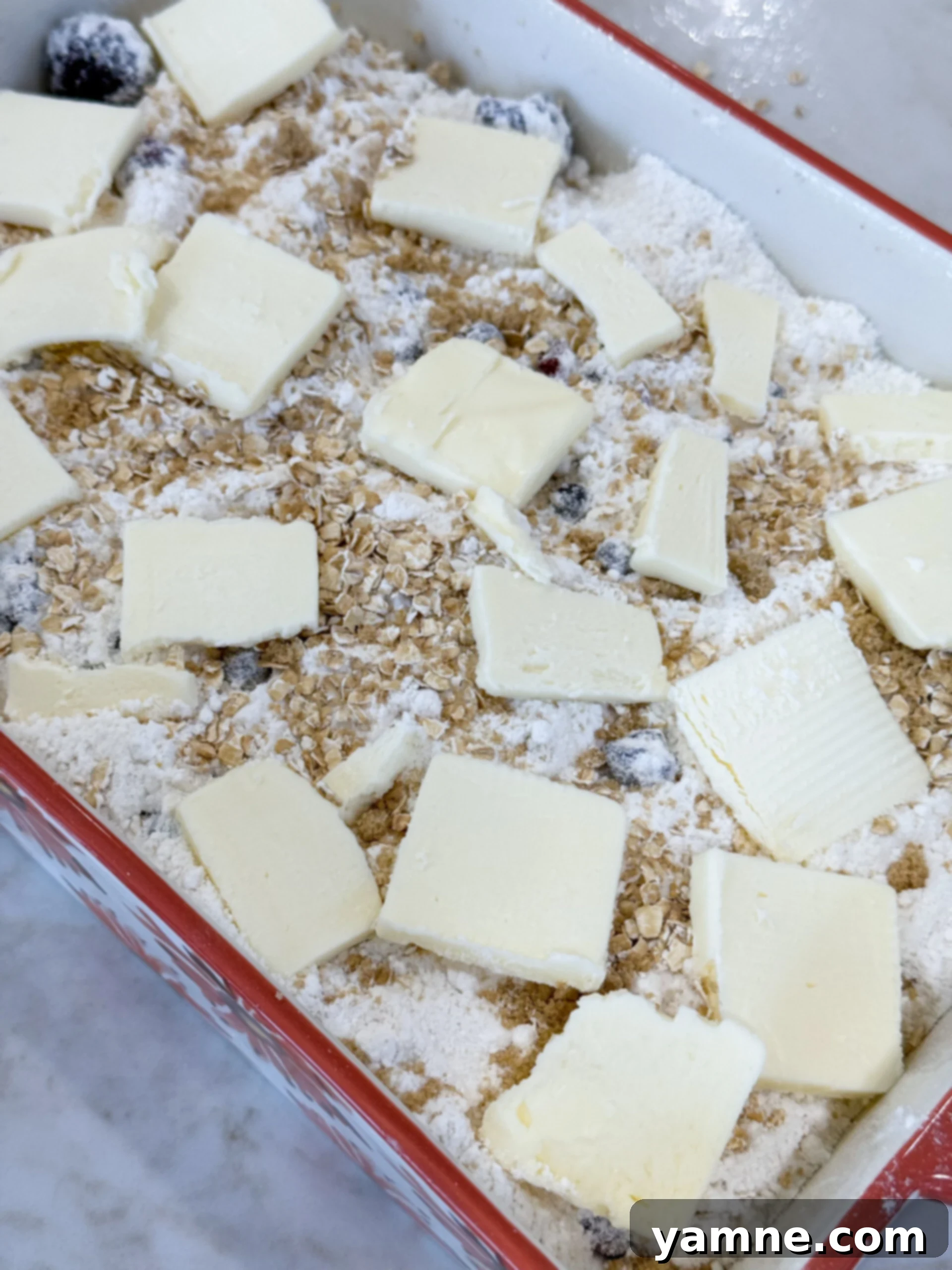 Adding sliced butter on top of berry cobbler before baking