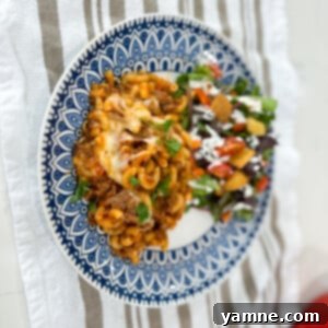 A close-up shot of a cheesy, saucy one-pot macaroni lasagna in a pan, garnished with fresh herbs.