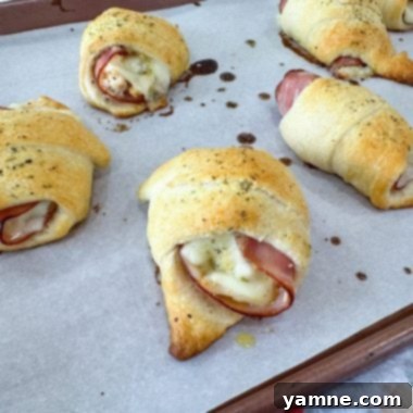Golden brown chicken cordon bleu pockets with melted Swiss cheese oozing out, on a baking sheet.