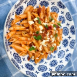 A close-up of creamy cheesy bacon pasta, garnished with fresh herbs, showcasing the rich sauce and crispy bacon bits.