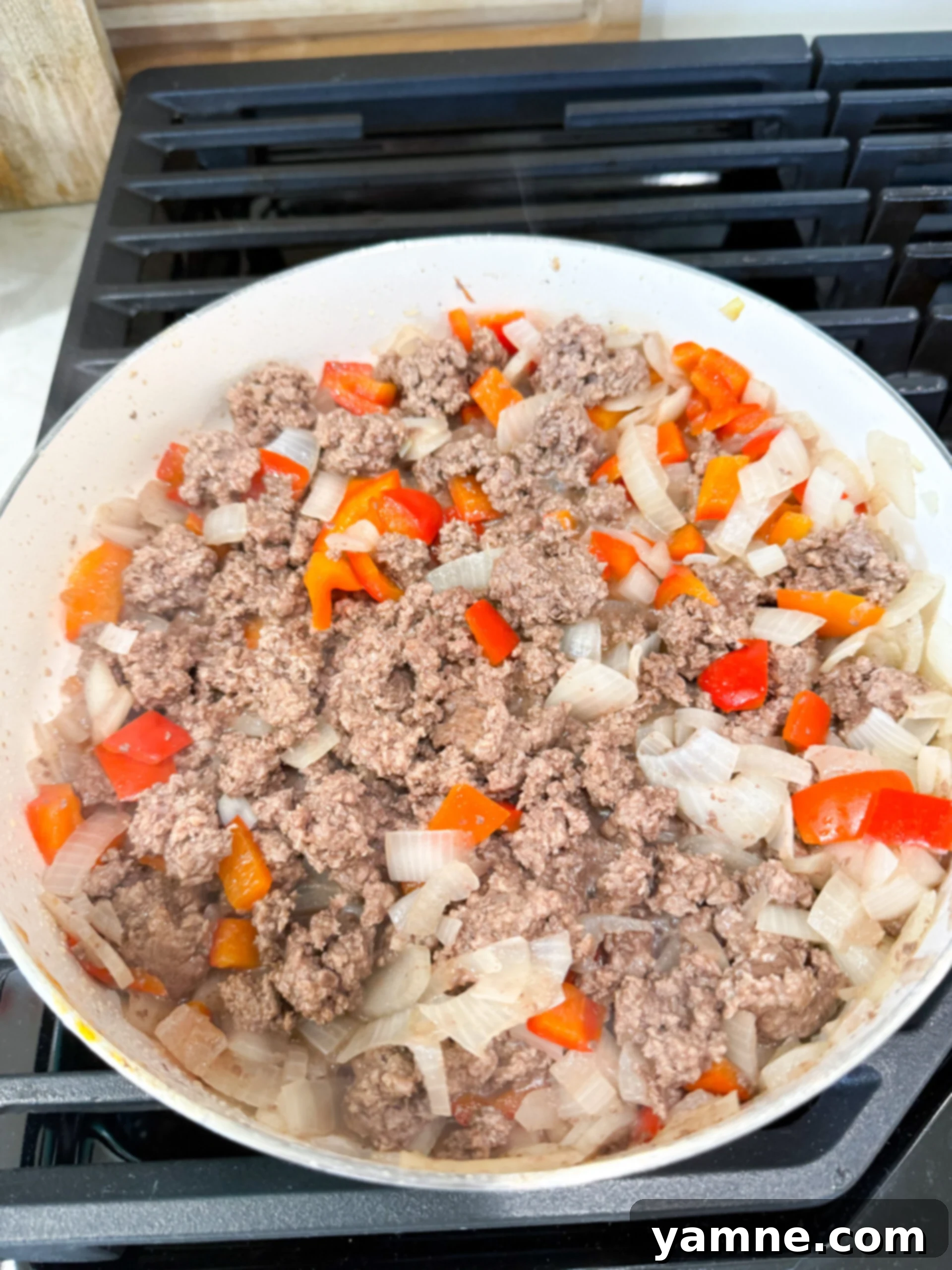 Ground beef, diced onion, and bell peppers cooking in a large skillet