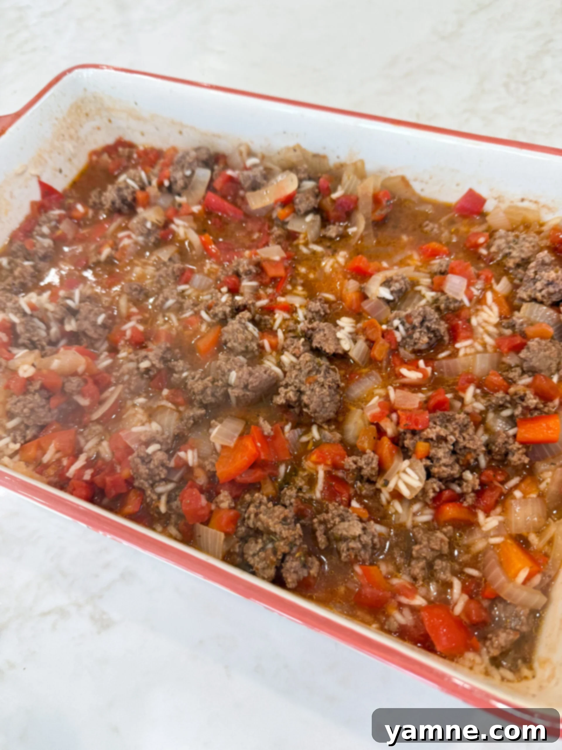 Stirring uncooked rice, browned beef, and cheese in a casserole dish before baking