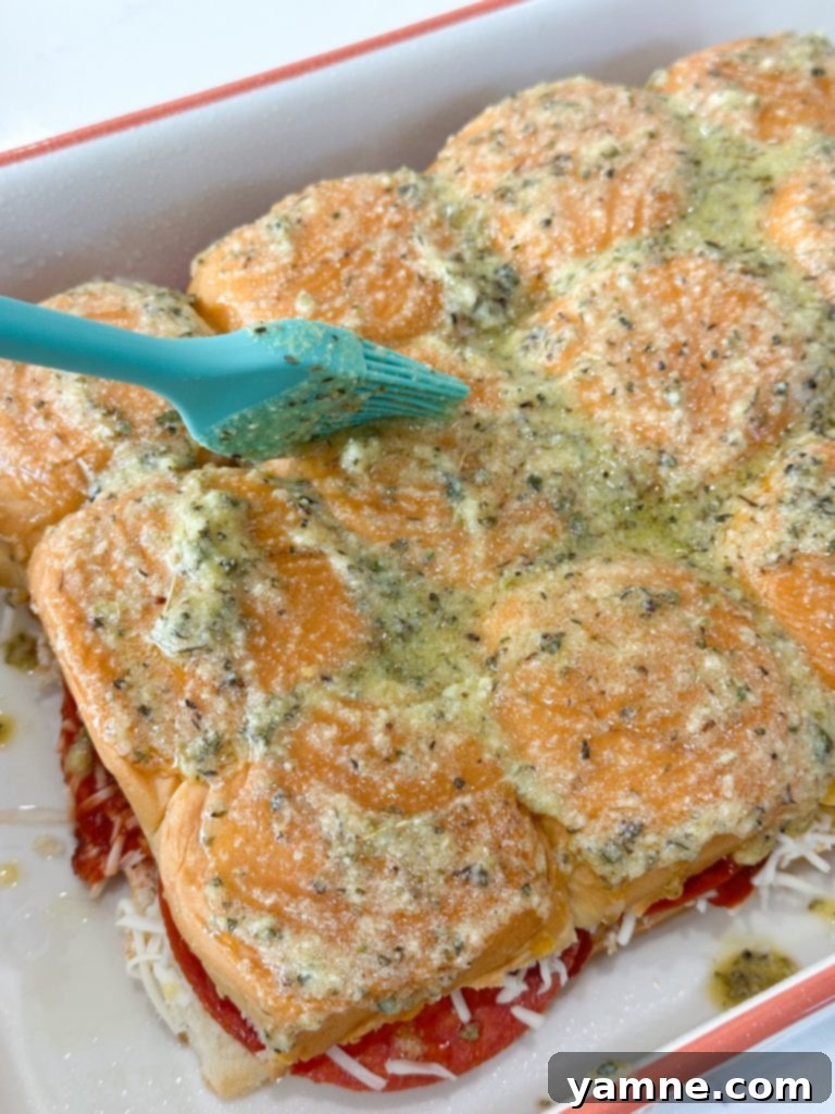 Assembled pizza sliders with layers of cheese, sauce, and pepperoni, topped with the other half of the Hawaiian rolls.