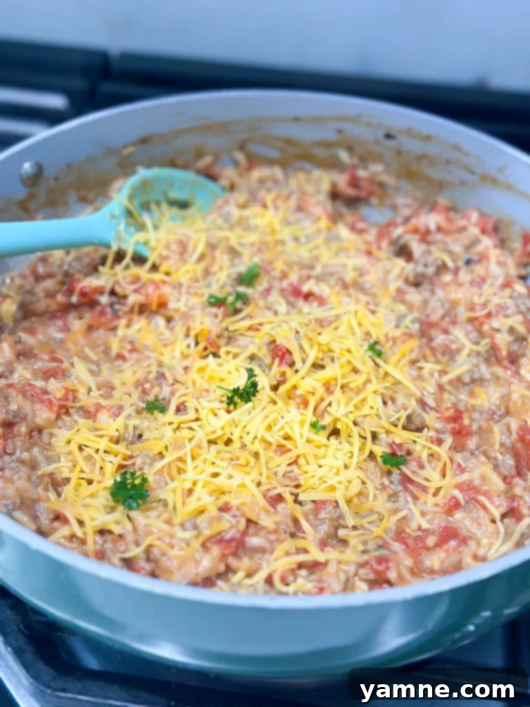 A skillet of hamburger rice casserole simmering on the stove, with the lid slightly ajar.