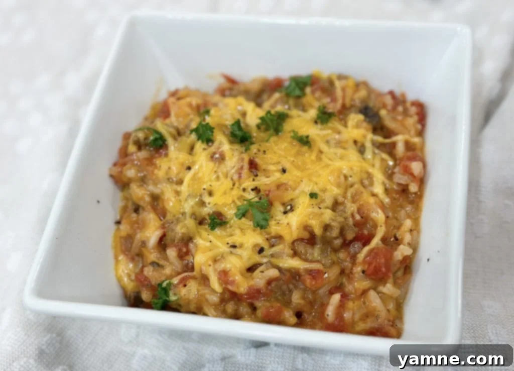 A spoonful of hamburger rice casserole being served from the skillet, showing the cheesy, meaty, and rice texture.