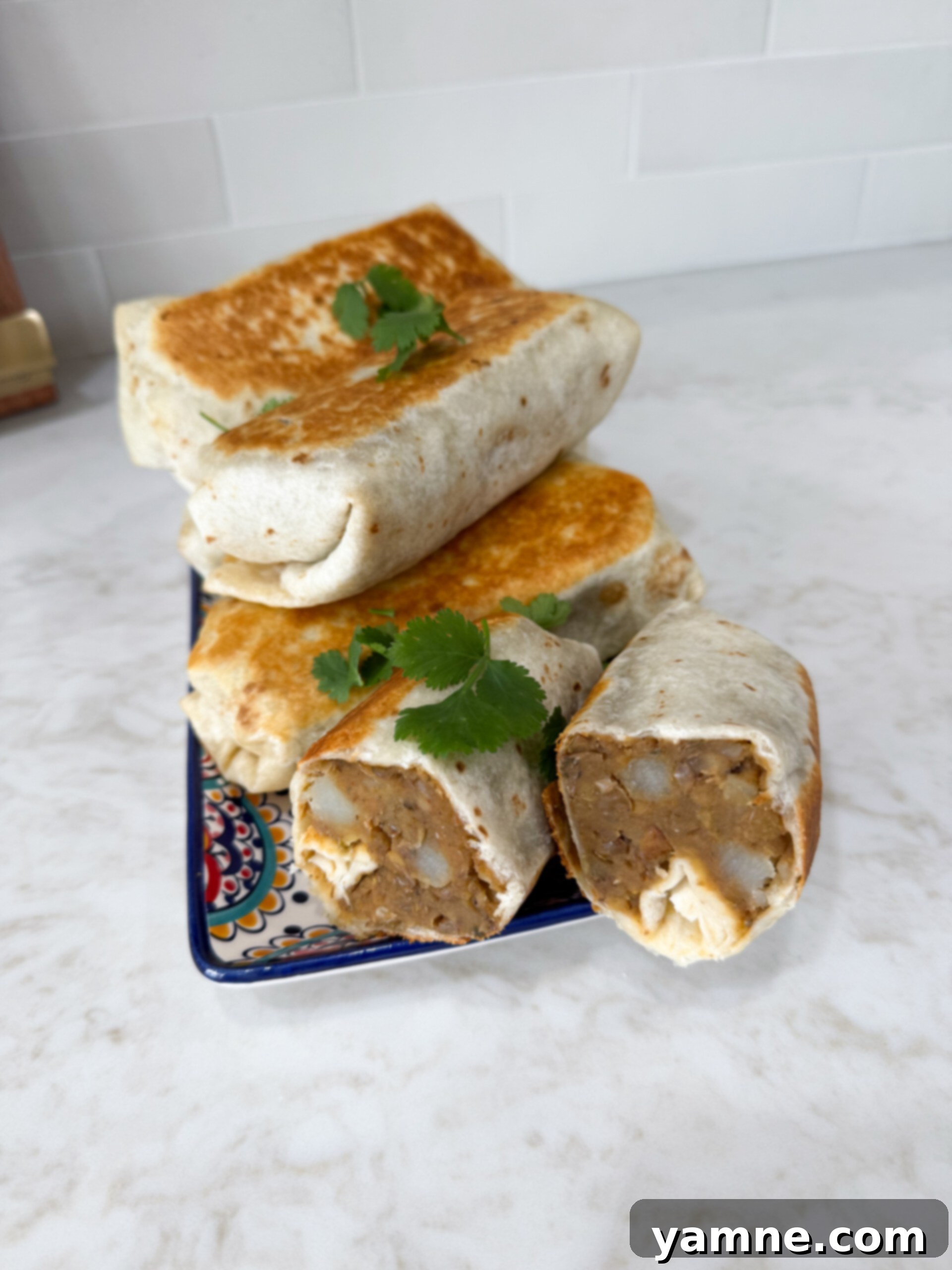 Hearty Lentil Potato Burritos 2 Stacked lentil and potato burritos on a white plate, showcasing their golden-brown exterior.