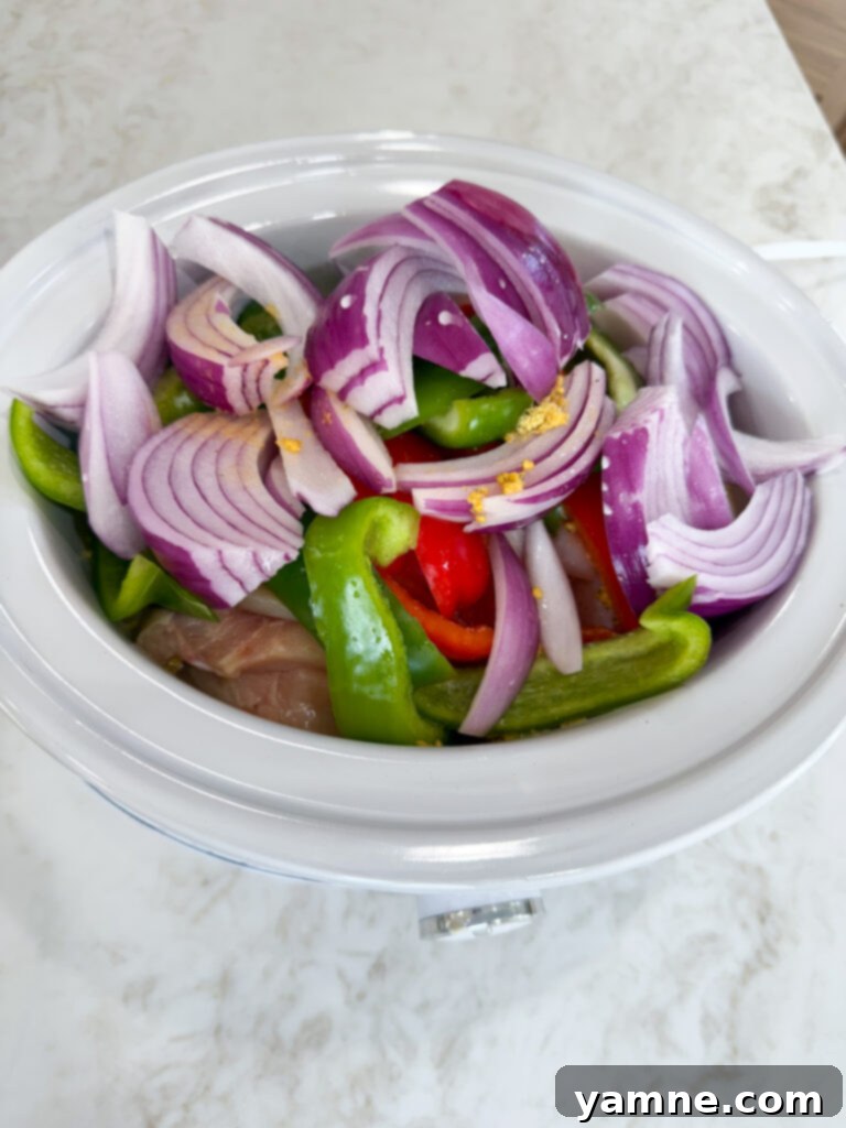 Adding all ingredients to the slow cooker for Crockpot Chicken Philly Cheesesteak Sandwiches