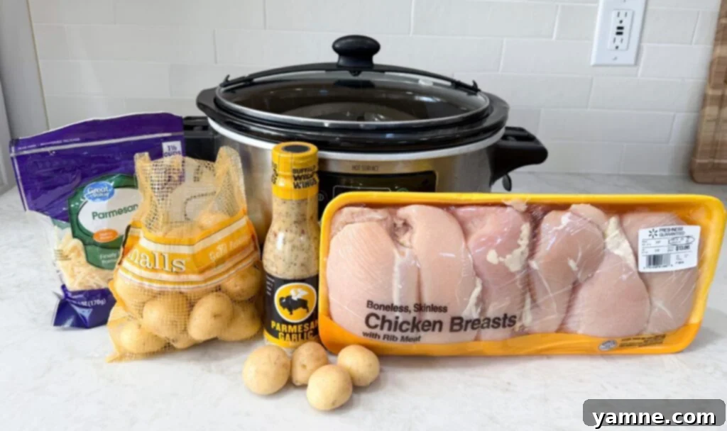 Comforting Slow Cooker Garlic Parmesan Chicken and Potatoes 4 Black and grey slow cooker on a counter with raw chicken, potatoes, with buffalo wing wings sauce and parmesan cheese