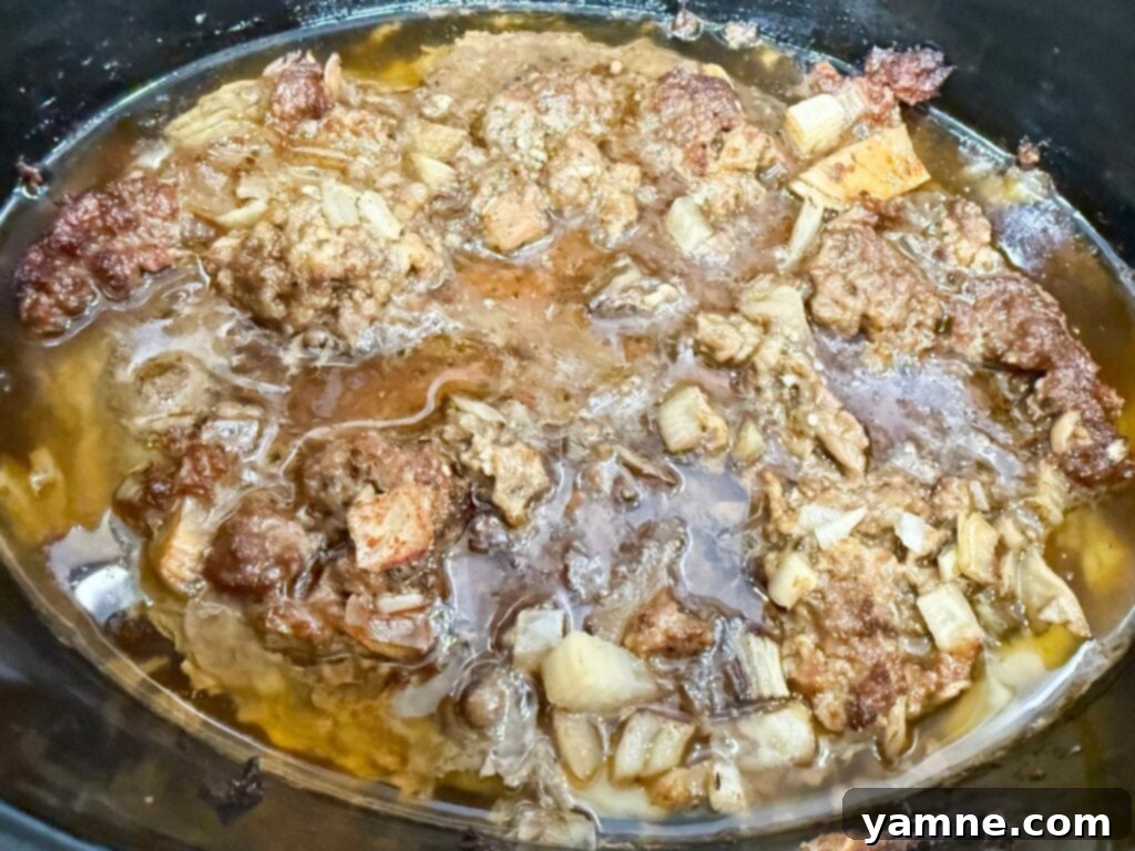 Cooked ground meat mixture in a black slow cooker, perfectly done and ready for draining.