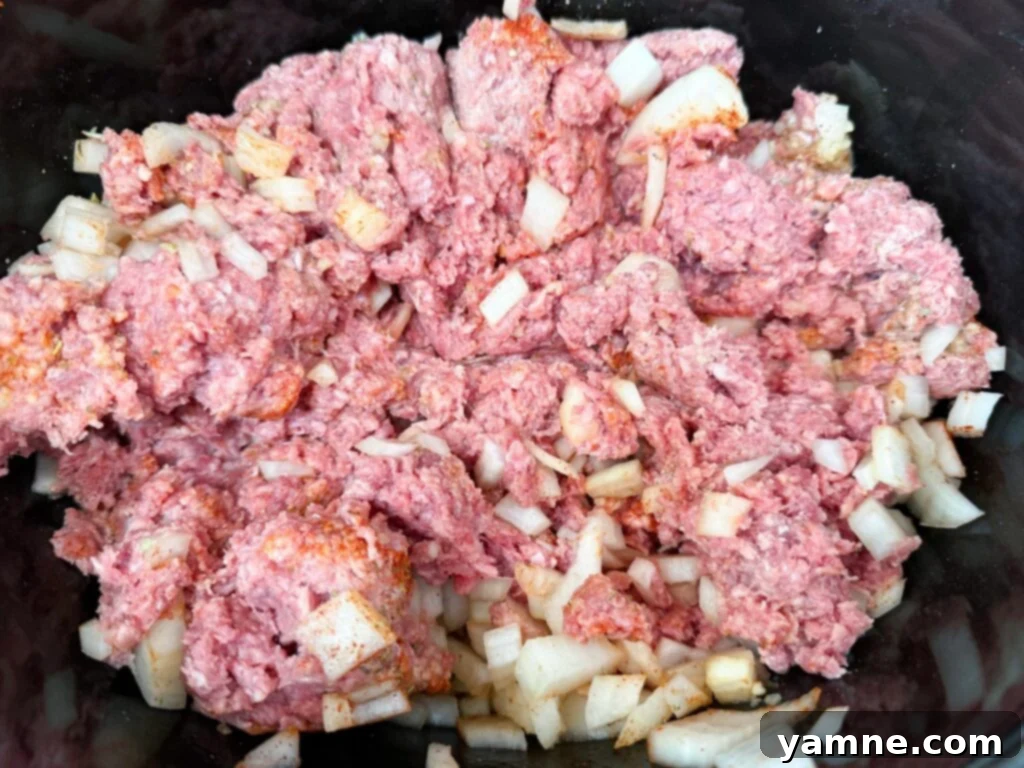Ground beef and onion mixture simmering in a black slow cooker, capturing the cooking process for tender slow cooker ground beef.