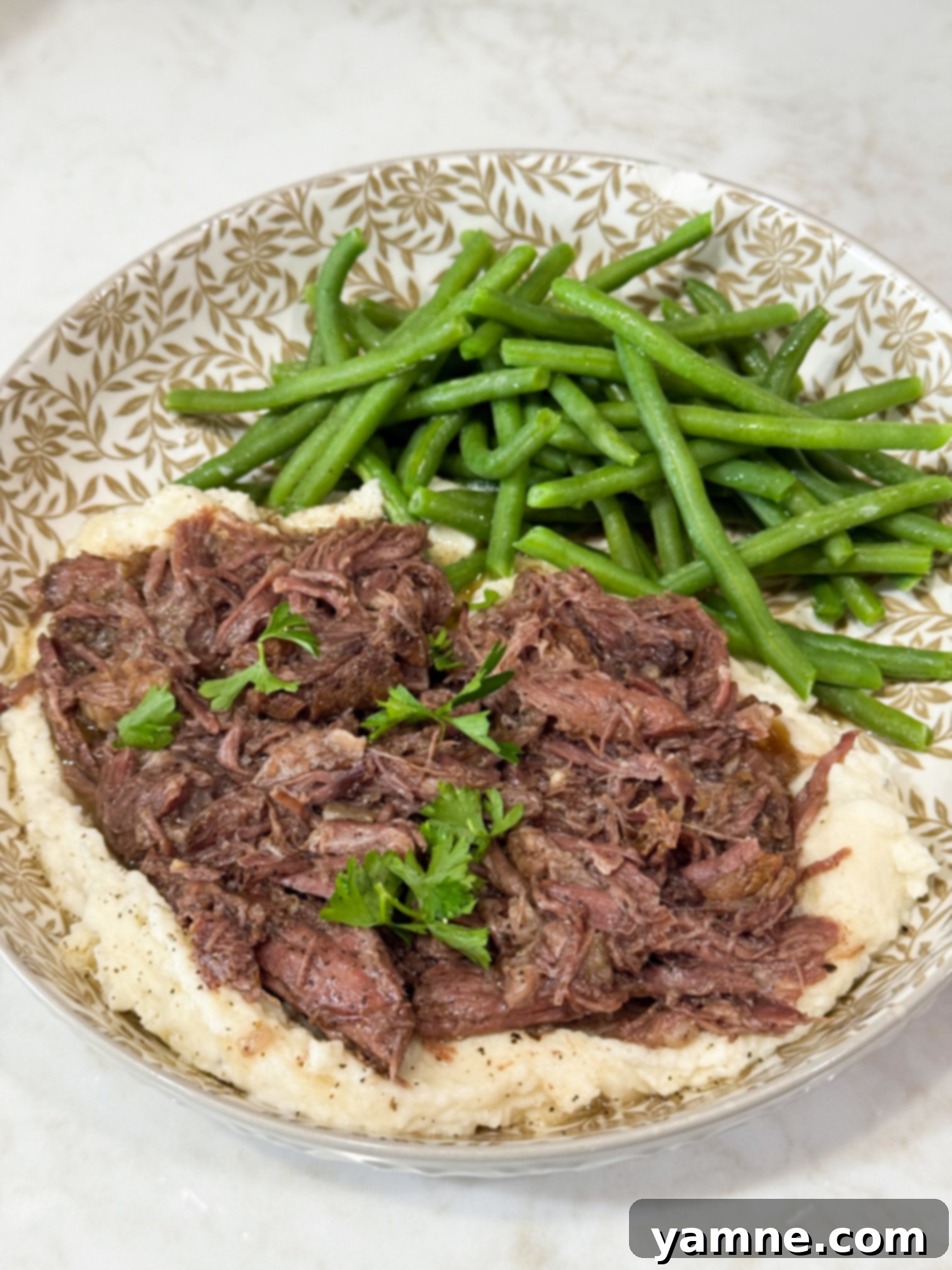 Slow Cooker Pulled Beef 2 Shredded beef over mashed potatoes with green beans on a grey and white plate