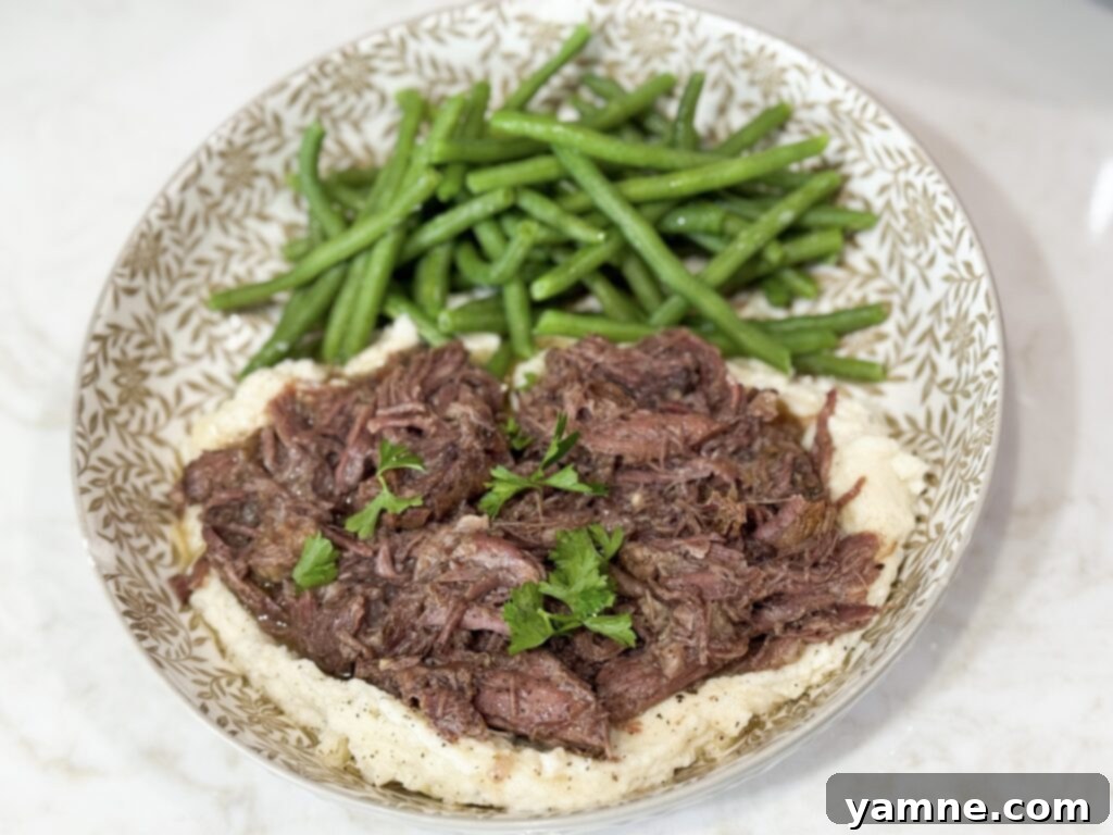 Slow Cooker Pulled Beef 7 Shredded beef over mashed potatoes with green beans on a grey and white plate