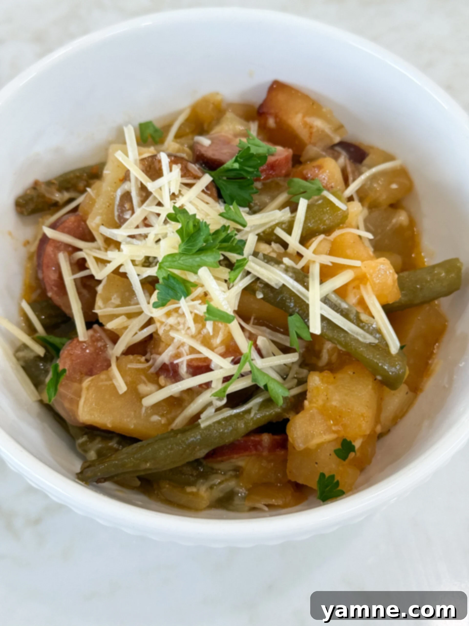 Cooked sausage, potatoes, and beans in a white bowl topped with parmesan cheese and fresh parsley