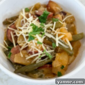 Cooked sausage, potatoes, and beans in a white bowl topped with parmesan cheese and fresh parsley