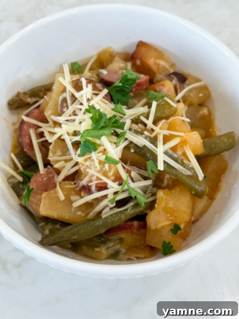 Cooked sausage, potatoes, and beans in a white bowl topped with parmesan cheese and fresh parsley
