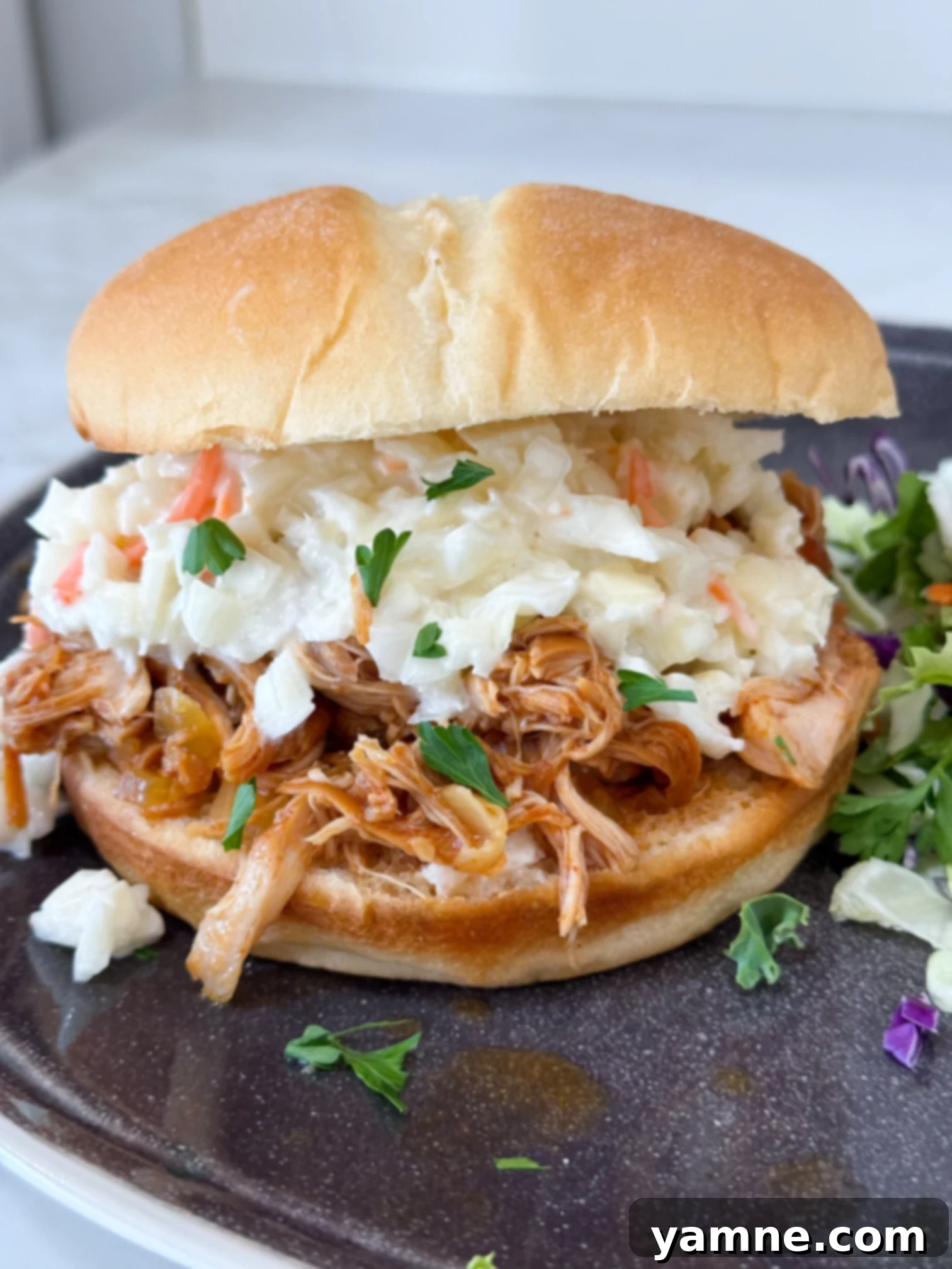 Slow cooker Hawaiian barbecue chicken sandwiches on a black plate with salad on a grey counter
