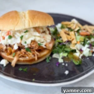 Slow cooker Hawaiian barbecue chicken sandwiches on a black plate with salad on a grey counter