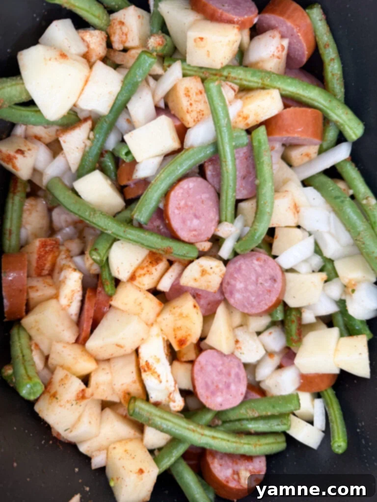 Prepped Kielbasa sausage, diced onions, potatoes, and green beans arranged neatly in a slow cooker before cooking.
