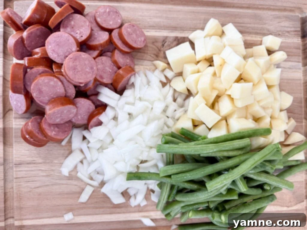 Chopped Kielbasa sausage, diced onions, potatoes, and fresh green beans neatly arranged on a cutting board, ready for the slow cooker.