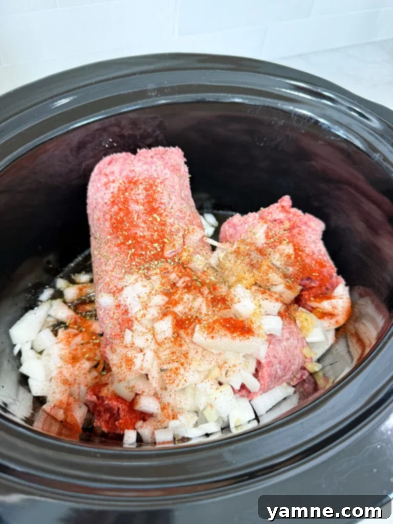 A black slow cooker filled with seasoned ground beef and onions, ready to simmer and become a versatile meal base.