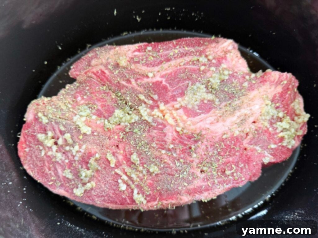 Seasoned beef roast prepared in a black slow cooker, promising tender shredded beef after cooking.