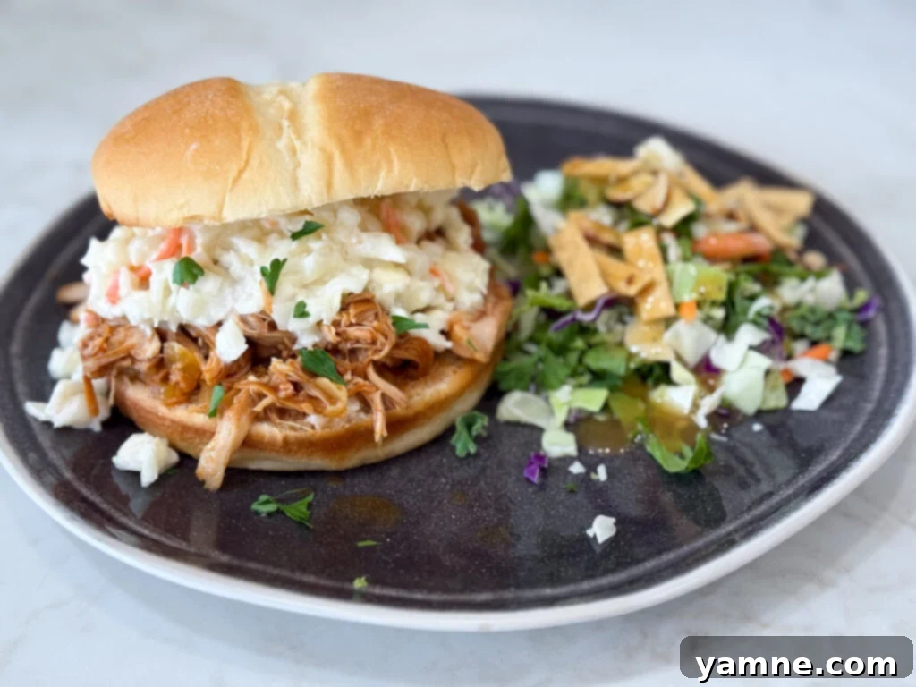 Delicious slow cooker Hawaiian barbecue chicken sandwiches served on dark plates with fresh green salad on a contrasting grey counter.