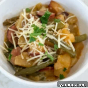 A hearty serving of cooked Kielbasa sausage, tender potatoes, and vibrant green beans in a white bowl, garnished with Parmesan cheese and fresh parsley.