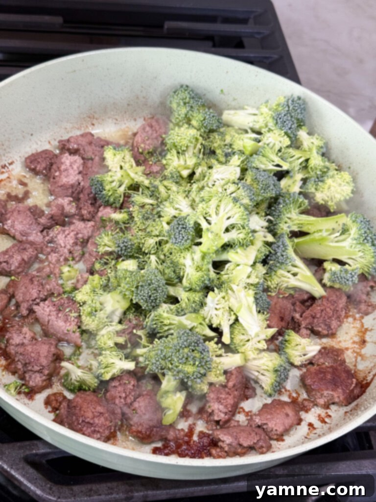 Cooked turkey in a pan with raw broccoli in a large skillet
