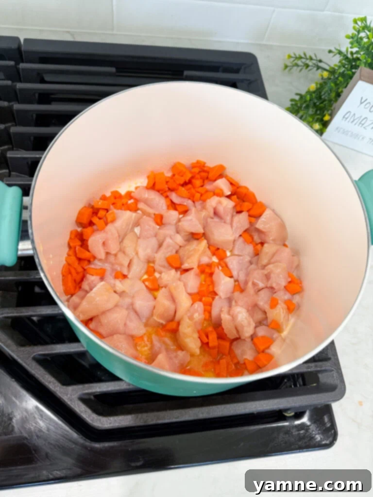 Velvety Chicken Noodle Bliss 4 Diced chicken, carrots, and onions sautéing in a pan with melted butter.