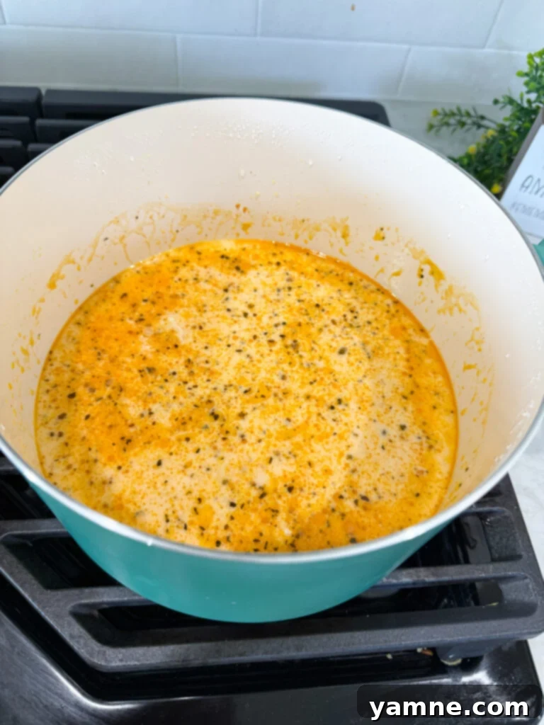 Velvety Chicken Noodle Bliss 5 Chicken broth being whisked into a roux with garlic in a pan.